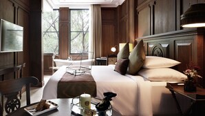 A well-appointed hotel room with a large bed, a desk with a lamp, a chair, a TV, and a view of the outdoors. - The Gunawarman (Jakarta)