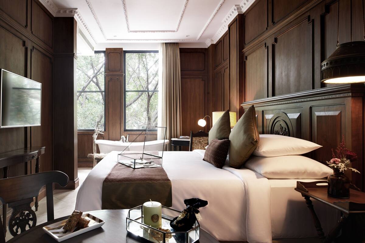 A well-appointed hotel room with a large bed, a desk with a lamp, a chair, a TV, and a view of the outdoors.