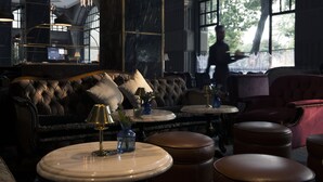 A luxurious interior with a dark-toned sofa, round tables, and leather ottomans. - The Gunawarman (Jakarta)