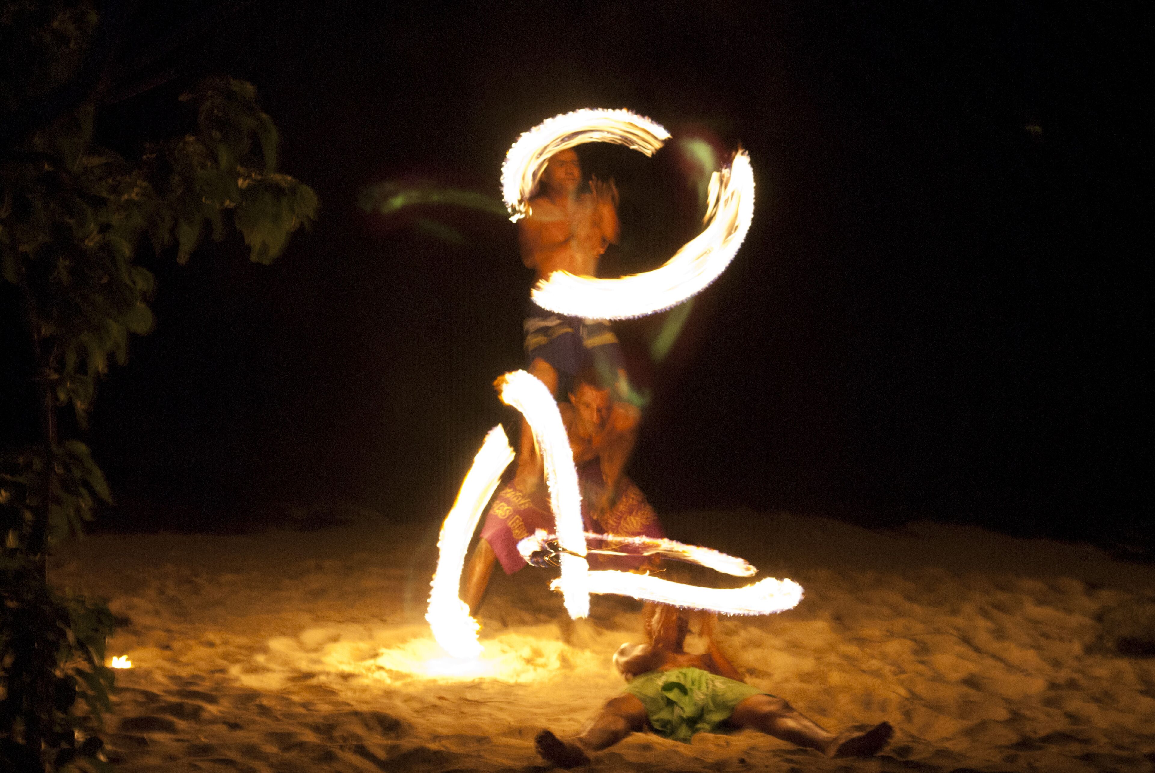 Una persona realizando malabares con fuego sobre arena de noche.