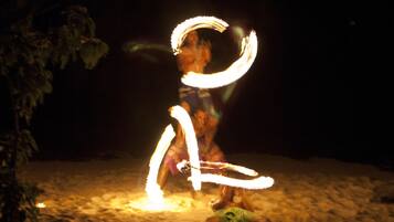 Una persona realizando malabares con fuego sobre arena de noche.