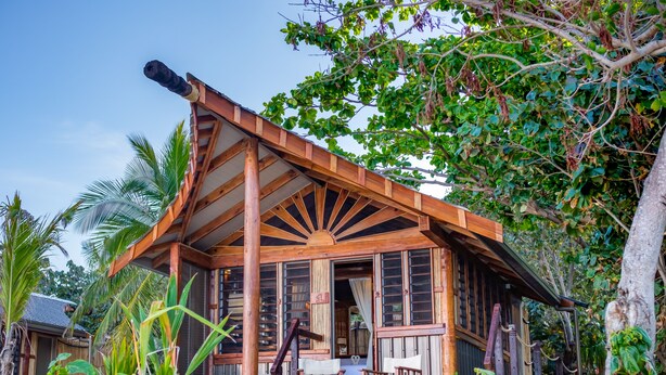 Ein Holzhaus mit Dachfenster, umgeben von tropischer Vegetation.