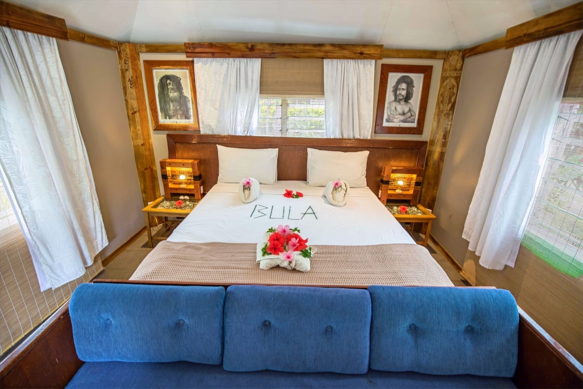 A bedroom with a large bed, two nightstands, a blue bench, and two framed pictures on the wall.