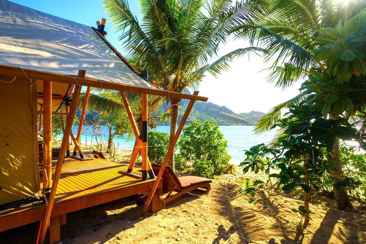 A beachside wooden structure with a deck, a covered area, and a view of the sea and mountains.