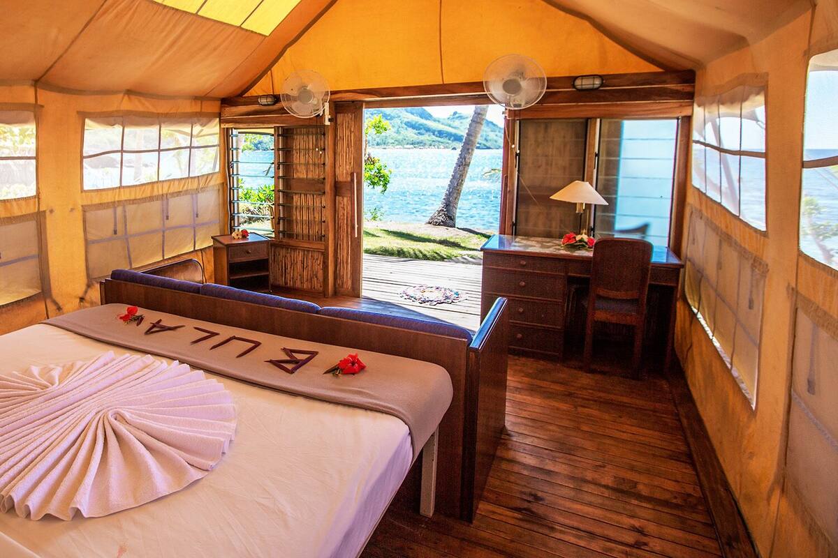 A tented room with a bed, a desk, and a view of the sea.
