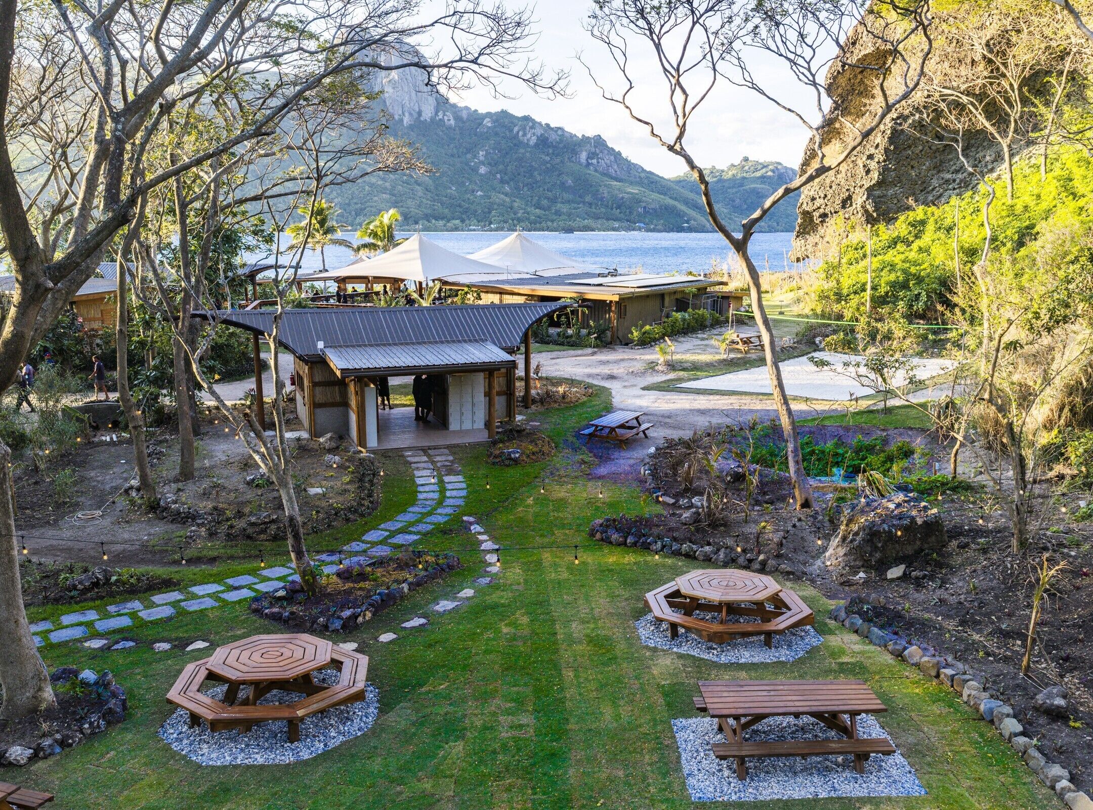 Un resort con un área al aire libre techada, mesas de picnic y vista al mar.