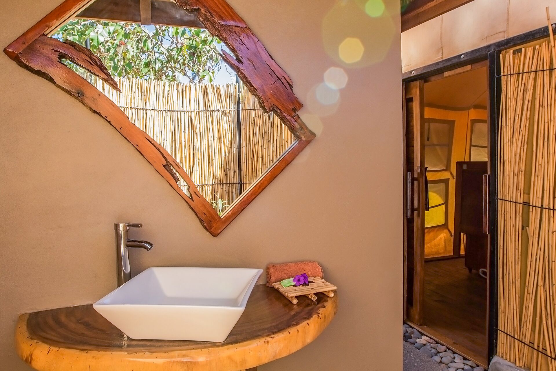 A bathroom with a wooden basin, a mirror, and a window with a bamboo backdrop.