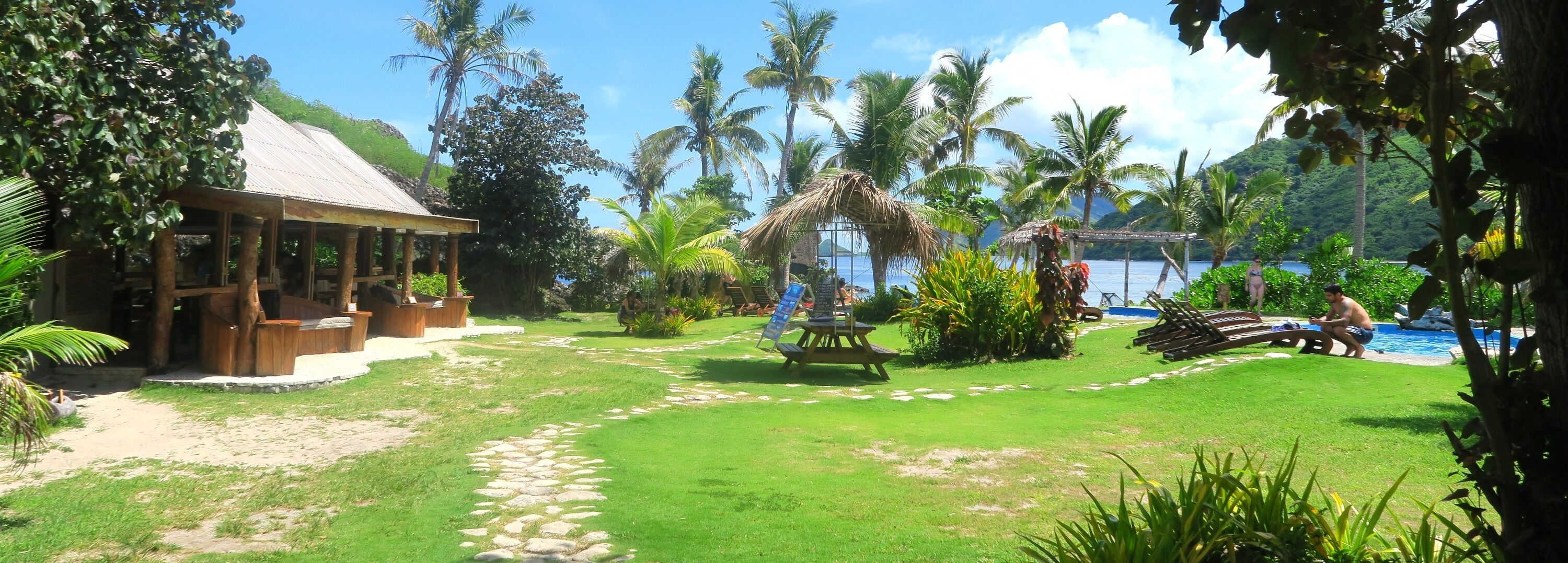 Un complexe hôtelier tropical doté d’une structure à toit de chaume, d’une piscine et d’une végétation luxuriante.