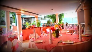 A banquet hall with round tables set for a meal, decorated with flowers and red tablecloths. - Hotel Sunrich Kandy (Hedeniya)