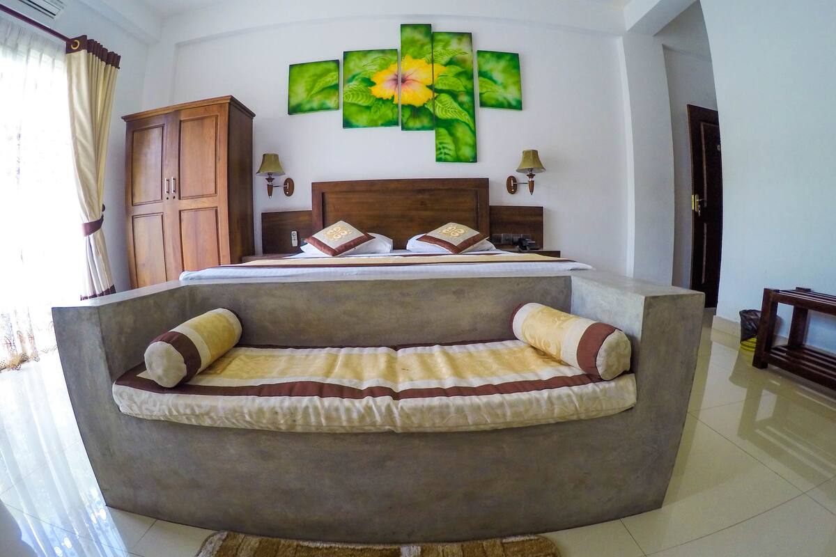 Ein Schlafzimmer mit einem Bett, einer Schlafcouch, einem Holzschrank und einer Wand mit drei floralen Gemälden.