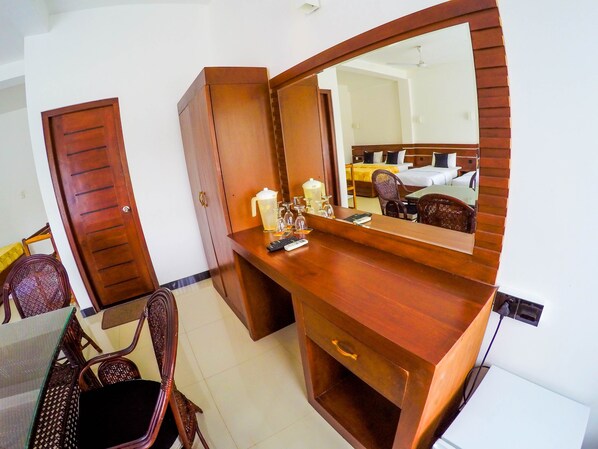 A hotel room with a wooden vanity, a large mirror, a bed with a yellow bedspread, and a chair.