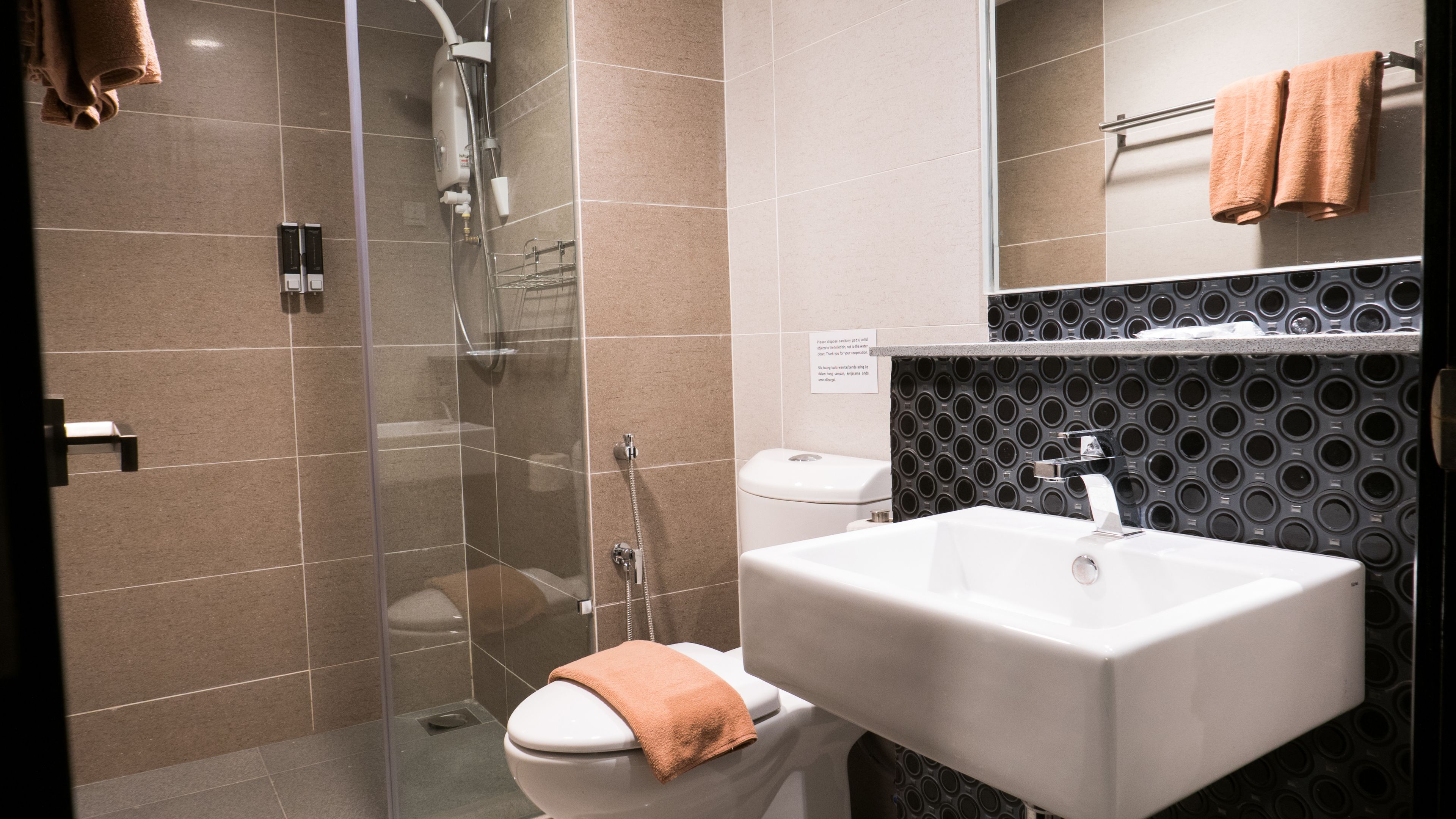 Een moderne badkamer met een douchecabine van glas, een wit toilet en een wastafel met een zwart patroon op de achterwand.