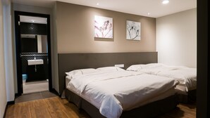 A hotel room with two beds, a bathroom with a sink, and two wall-mounted artworks.