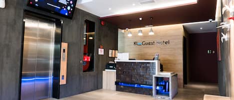 A modern hotel reception area with a digital display, a reception desk, and an elevator.