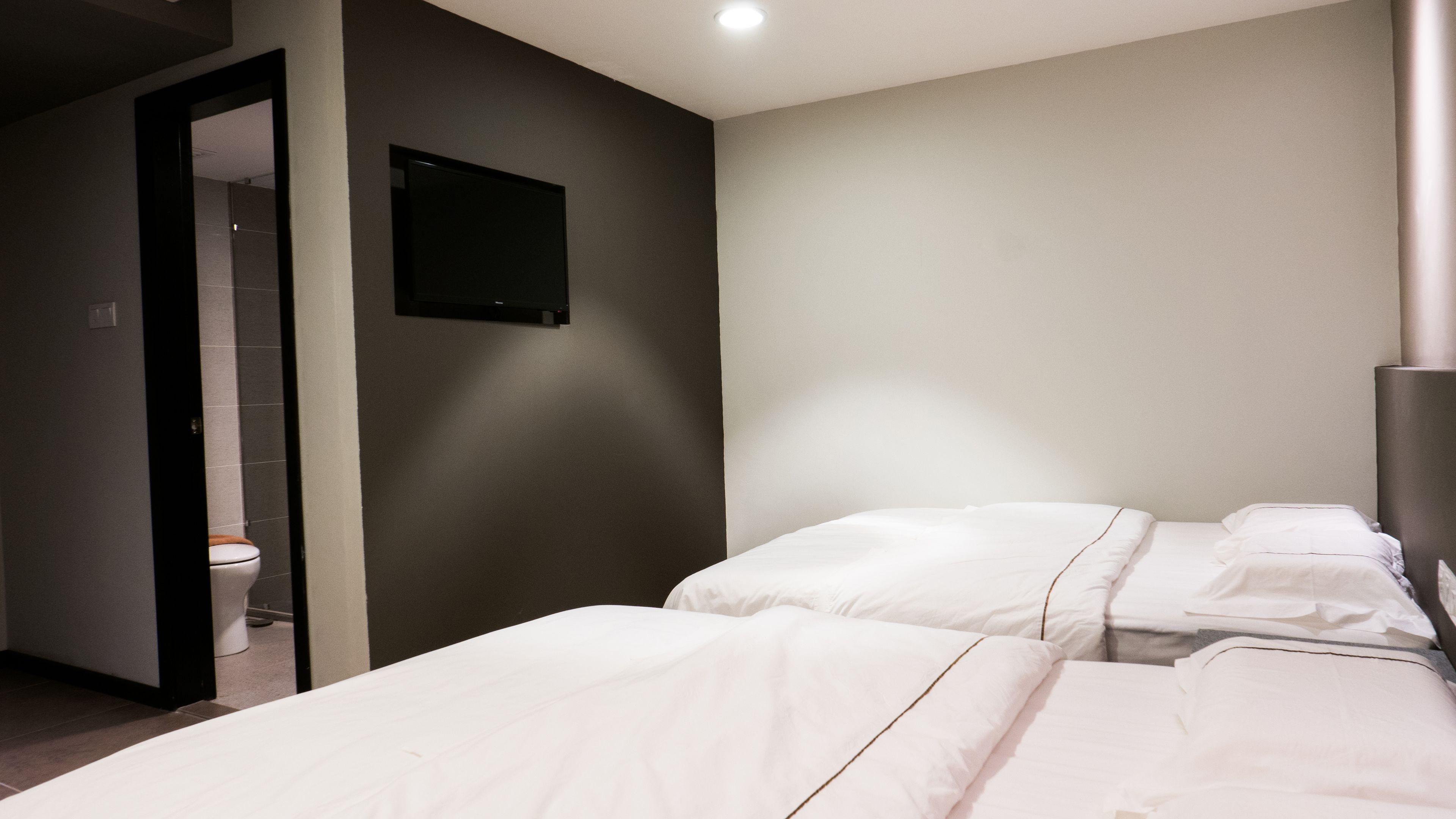 Quarto de hotel com uma cama, televisão fixada na parede e porta para um banheiro.