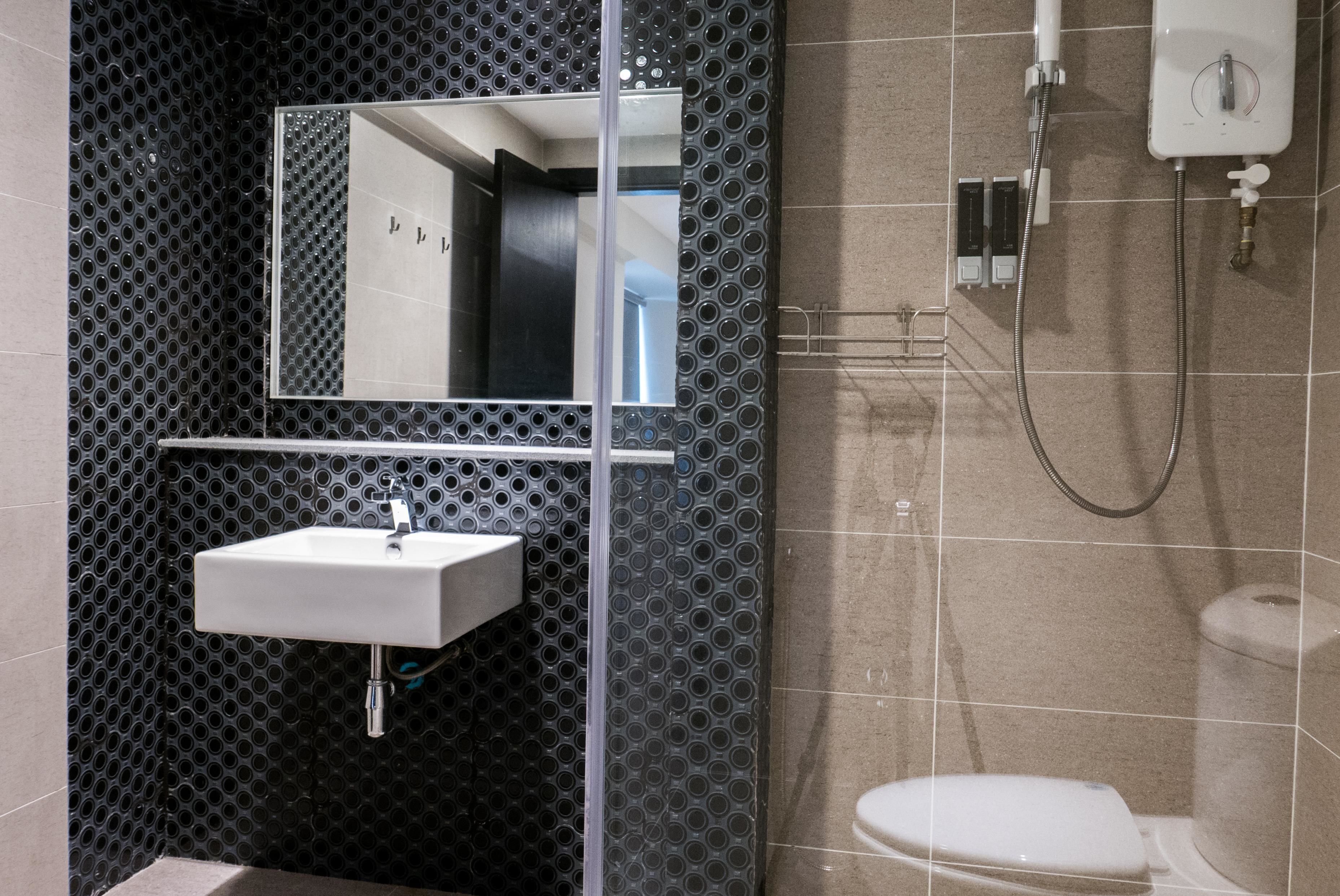 Un baño moderno con una pared perforada negra, un lavamanos blanco, un espejo y una ducha.