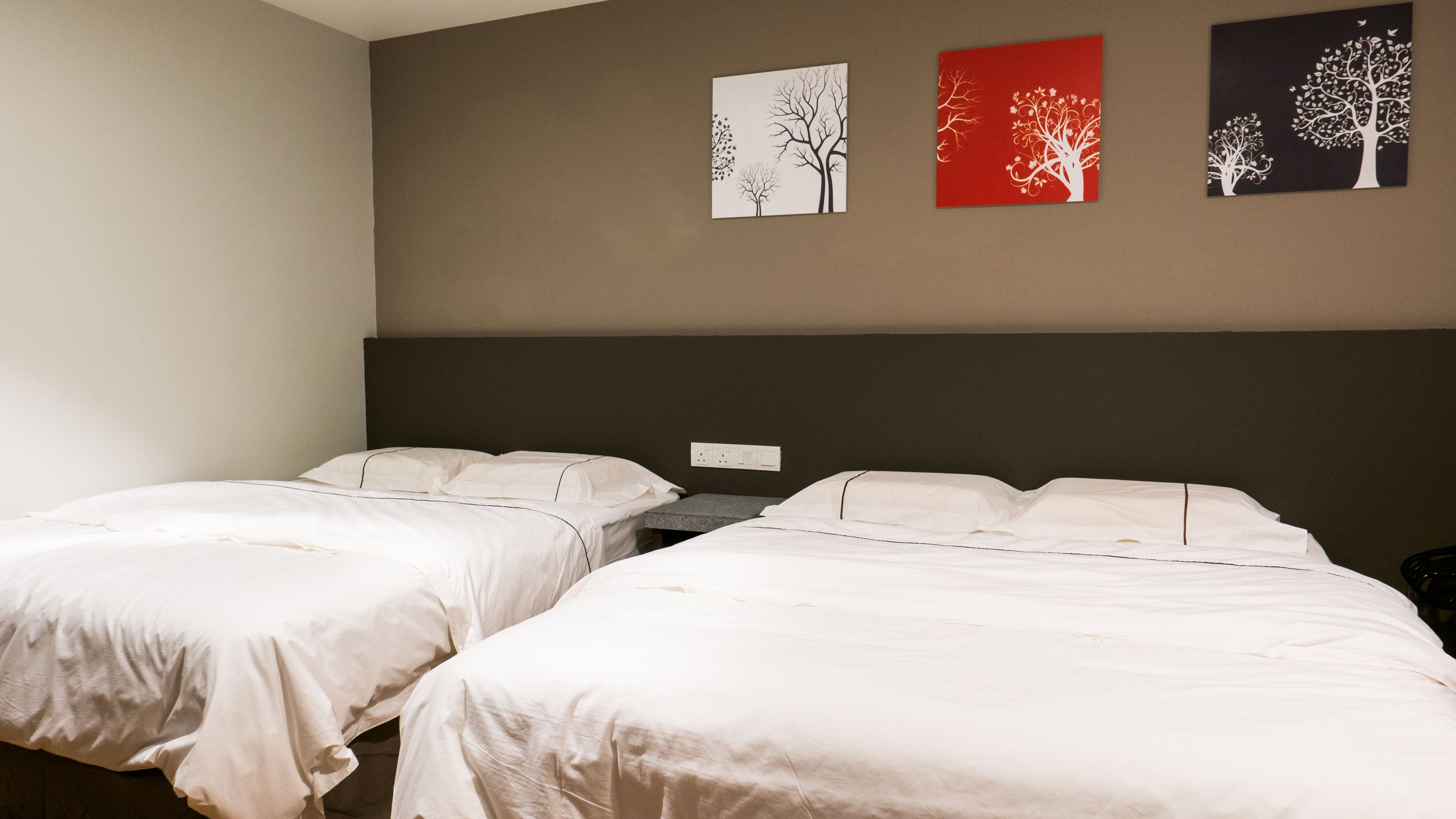 A hotel room with two beds, a dark headboard, and three wall art pieces depicting trees.