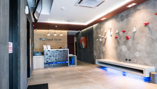 A modern hotel reception area with a wooden reception desk, a wall-mounted art piece, and a seating area with a bench.