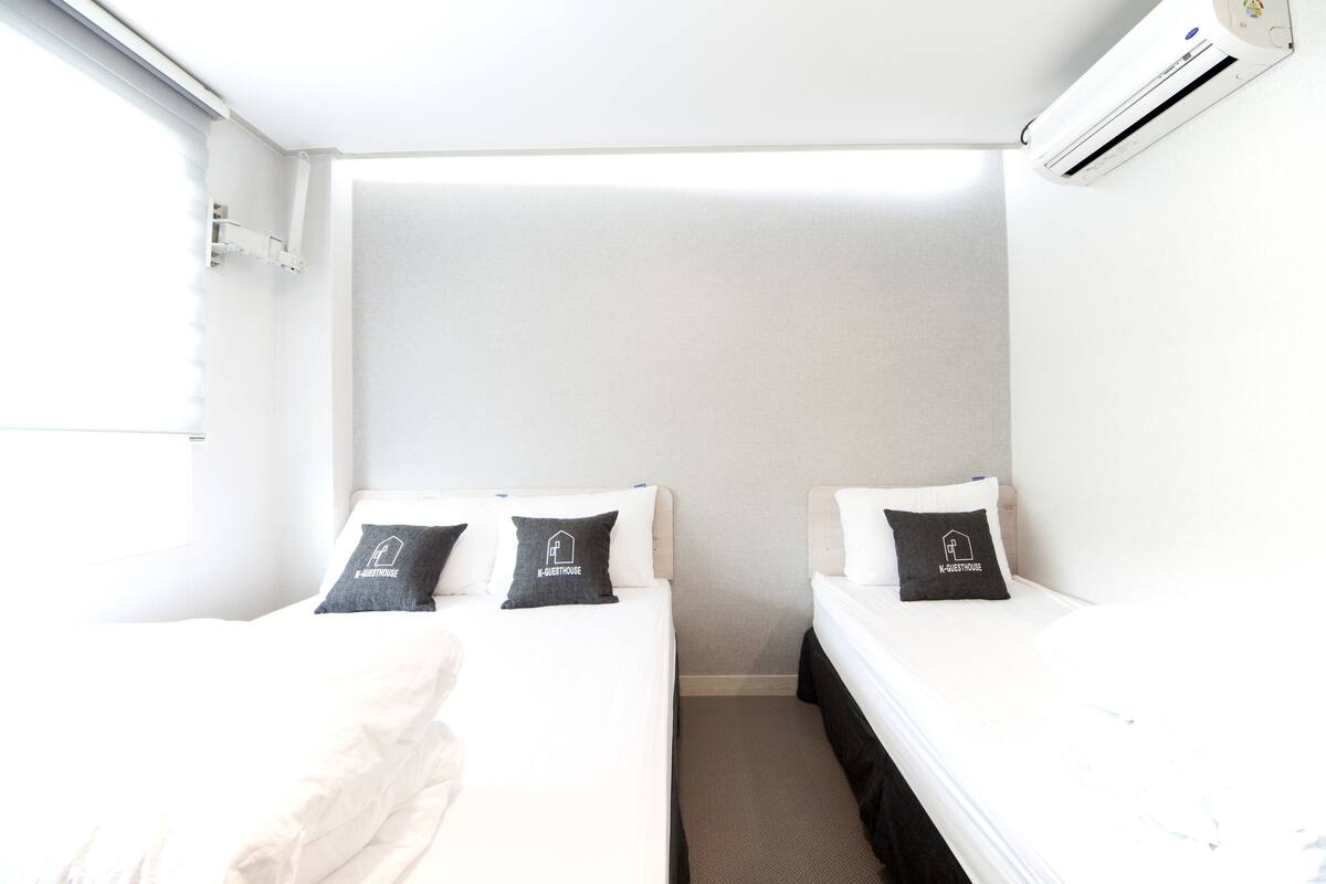A small, bright room with two beds, each with a pillow featuring a logo.