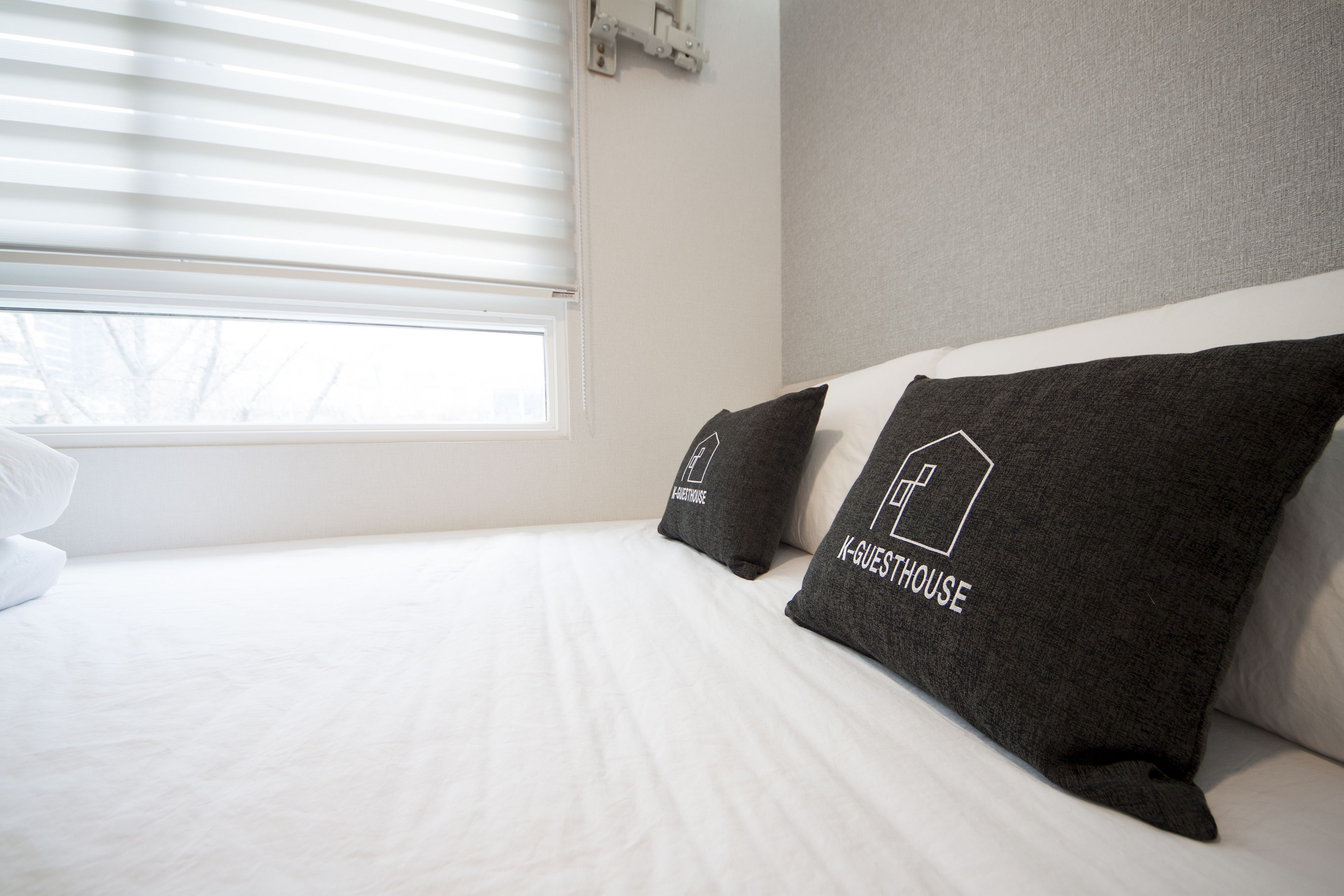 A neatly made bed with white linens and two dark gray pillows with white text.