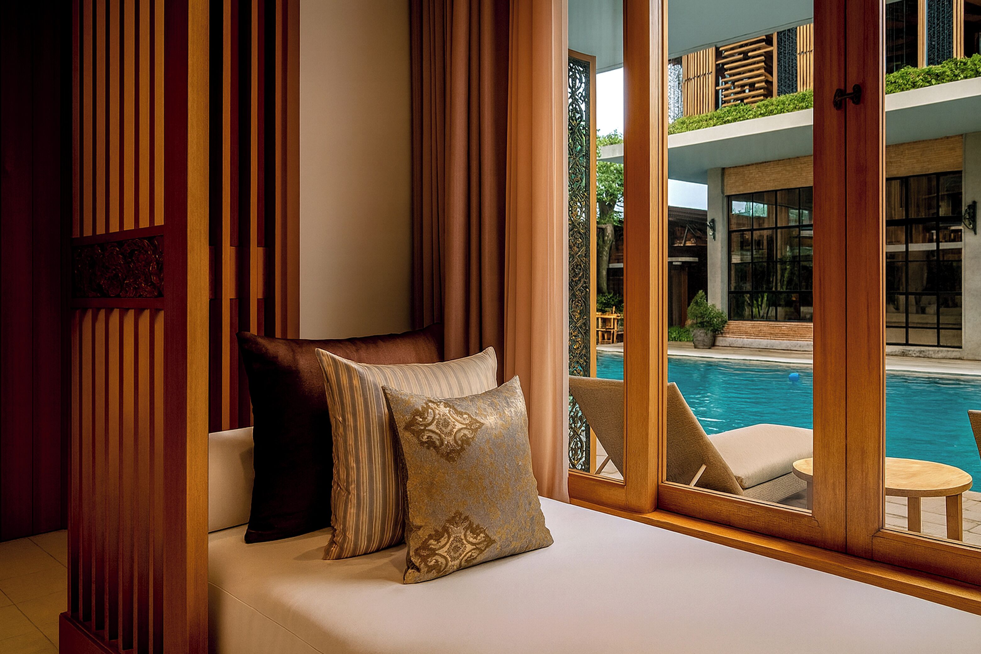 A room with a view of a swimming pool, a sofa with cushions, and a wooden partition.
