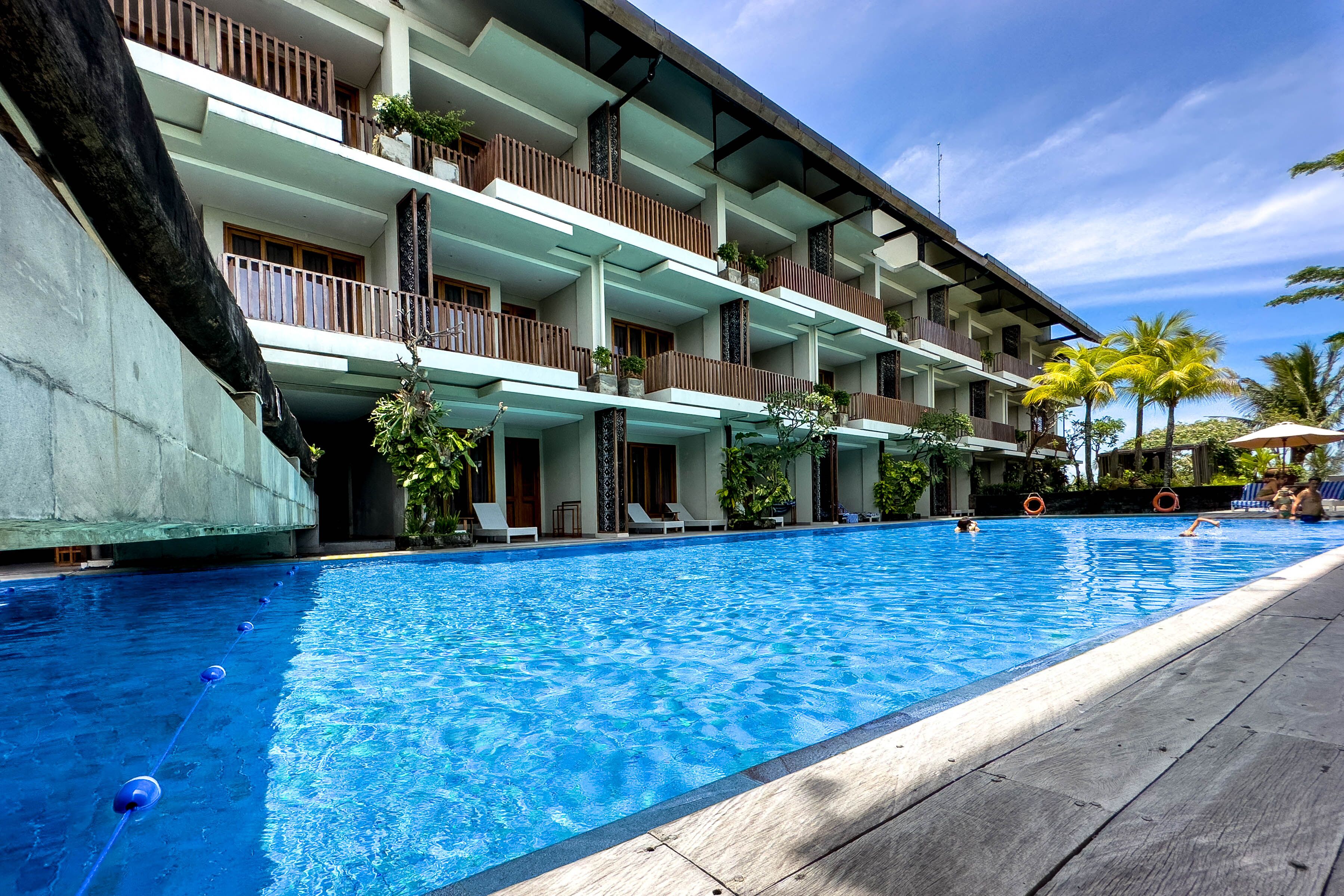 Un hotel con piscina, varios balcones y zonas de estar al aire libre.