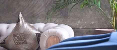 A plush sofa with decorative pillows and a potted plant in a room with a stone wall.