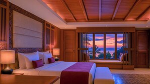 A hotel room with a large bed, a seating area by the window, and a view of the sunset.