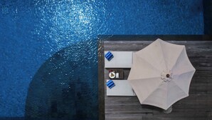 An aerial view of a swimming pool with a wooden deck, a white umbrella, and two blue towels.