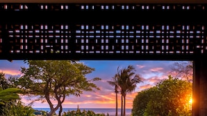 A wooden deck with two rocking chairs facing a sunset view over a garden and ocean.