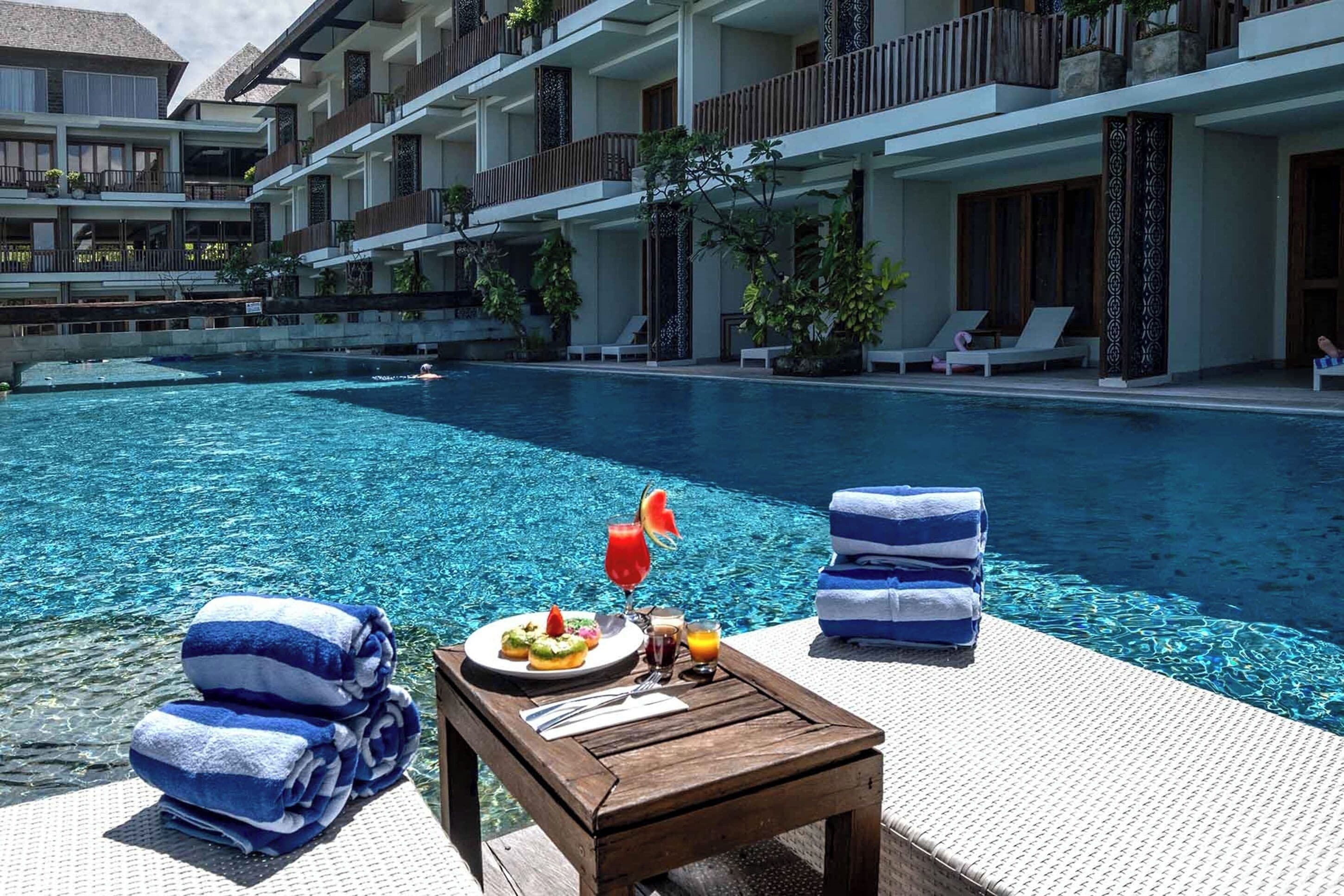 A poolside area with a wooden table, towels, and a plate of food.