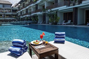 A poolside area with a wooden table, towels, and a plate of food.