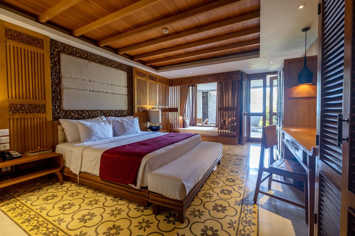 Een ruime slaapkamer met een groot bed, een houten hoofdeinde en een bureau met een stoel.