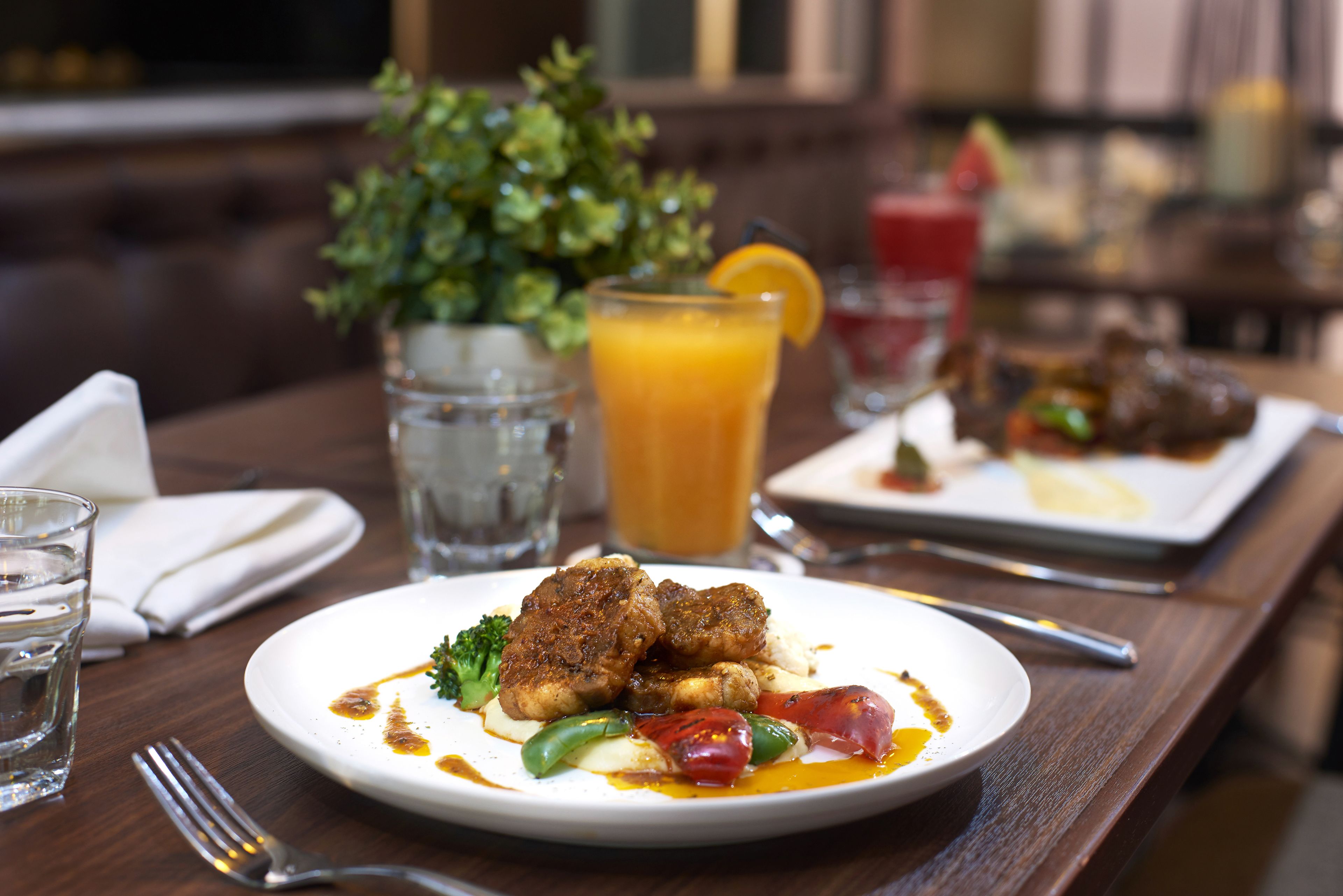A dining table with a plate of food, a glass of orange juice, and a glass of red drink.
