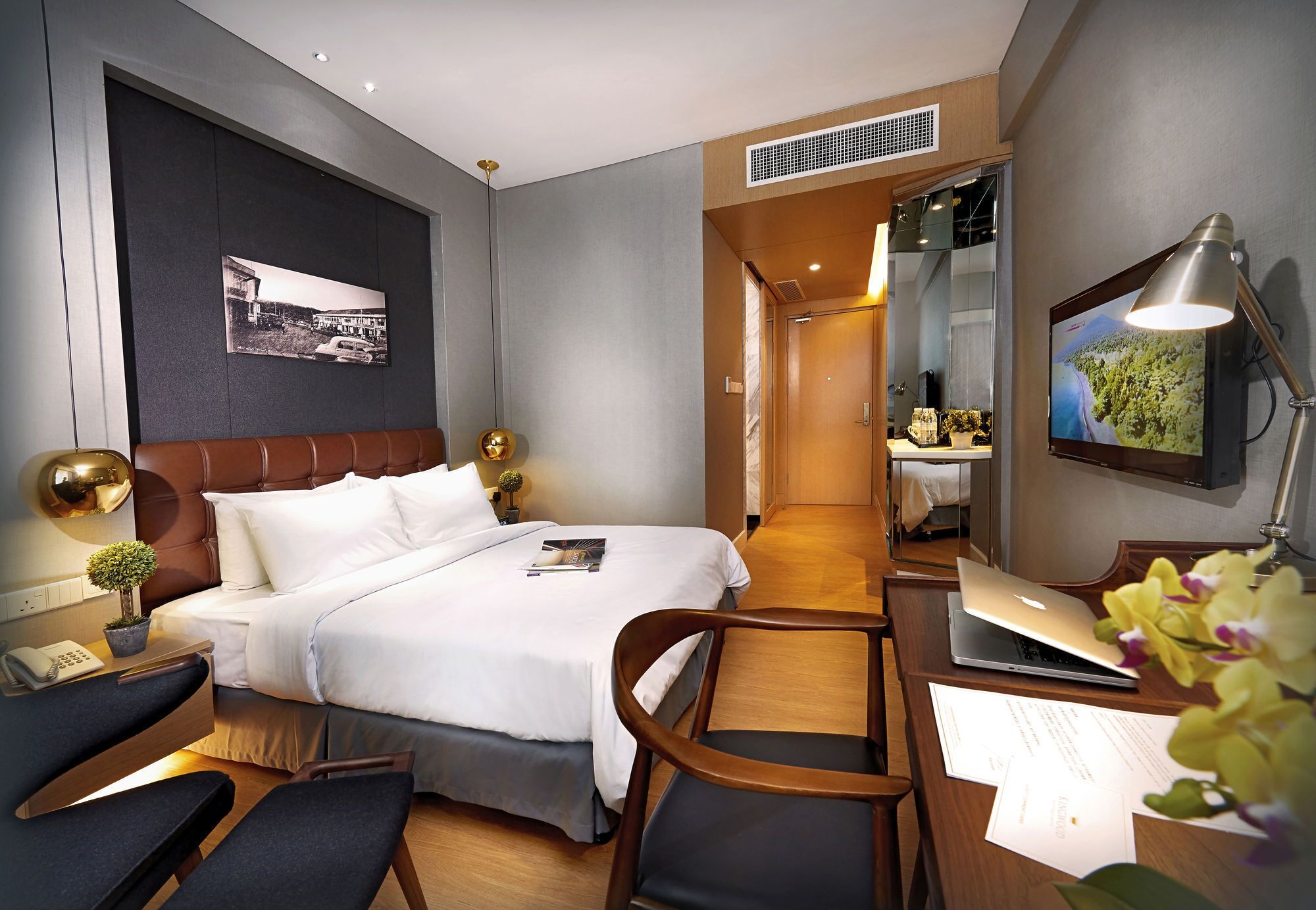 A modern hotel room with a bed, desk, chair, and a laptop.