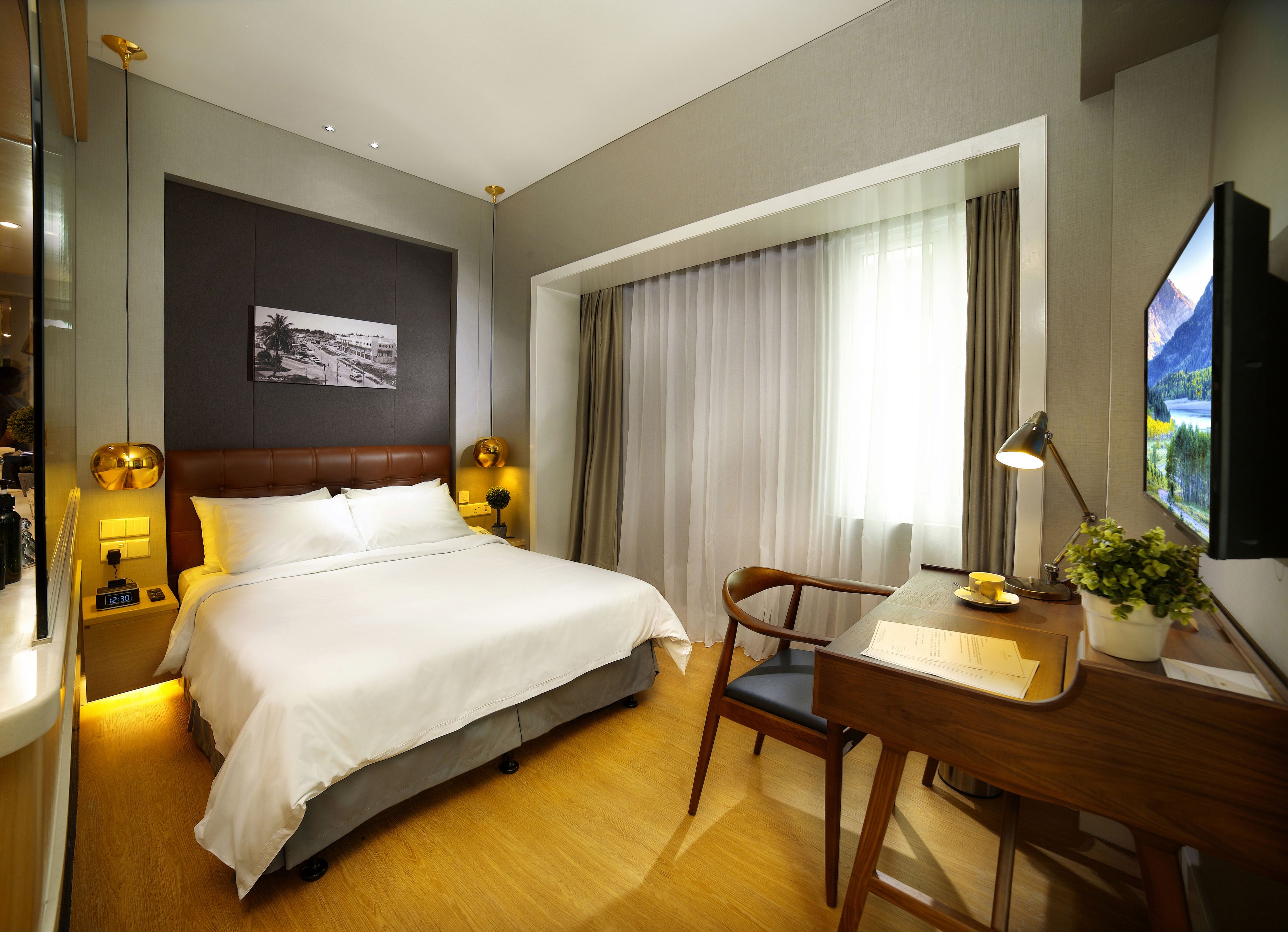 Une chambre d’hôtel avec un lit, un bureau, une chaise, une télévision et une fenêtre avec des rideaux.