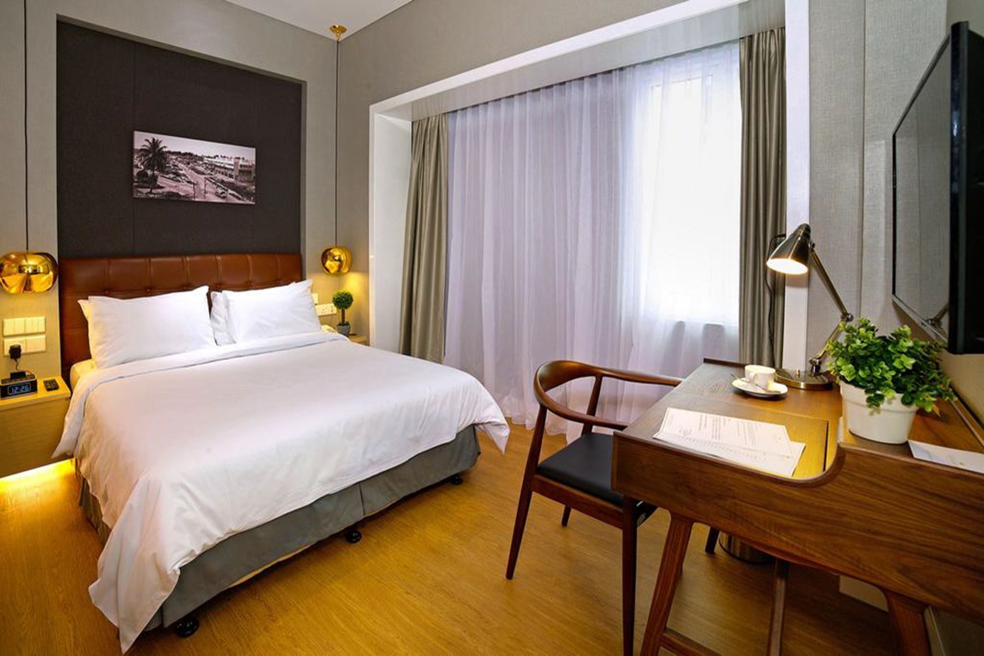 Habitación de hotel con cama, escritorio con silla, televisor, ventana con cortinas y un cuadro colgado en la pared.
