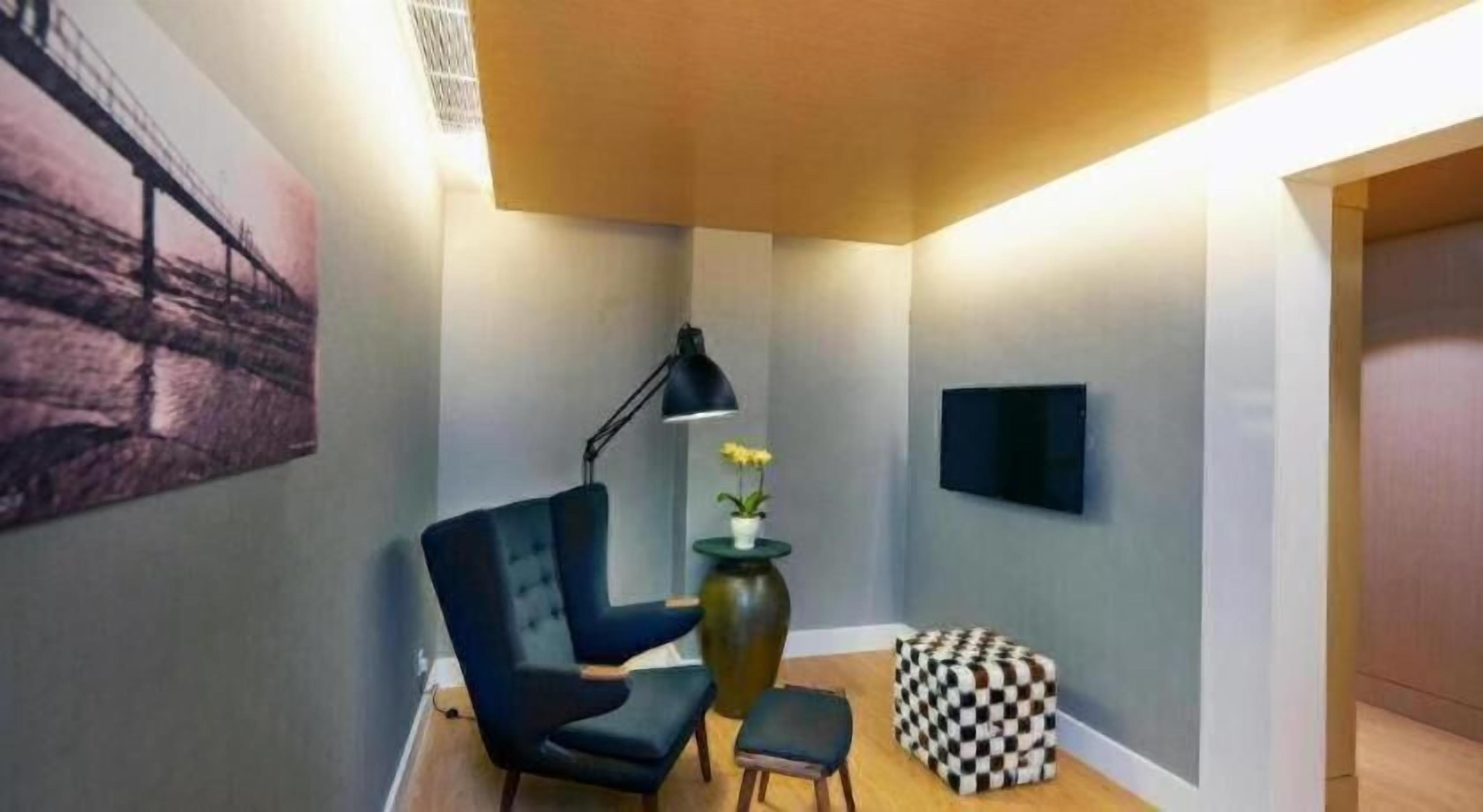 A modern interior with a dark blue armchair, a small table with a vase, and a checkered ottoman.