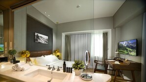 Ein Hotelzimmer mit einem großen Bett, einem Schreibtisch mit Stuhl, einem Fernseher und einem Badezimmer mit Waschbecken und Spiegel.