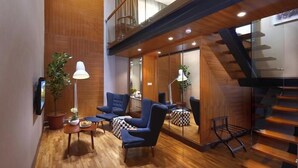 Ein modernes Interieur mit Holzboden, blauen Sesseln, einem kleinen Tisch mit Lampe und einer Treppe.