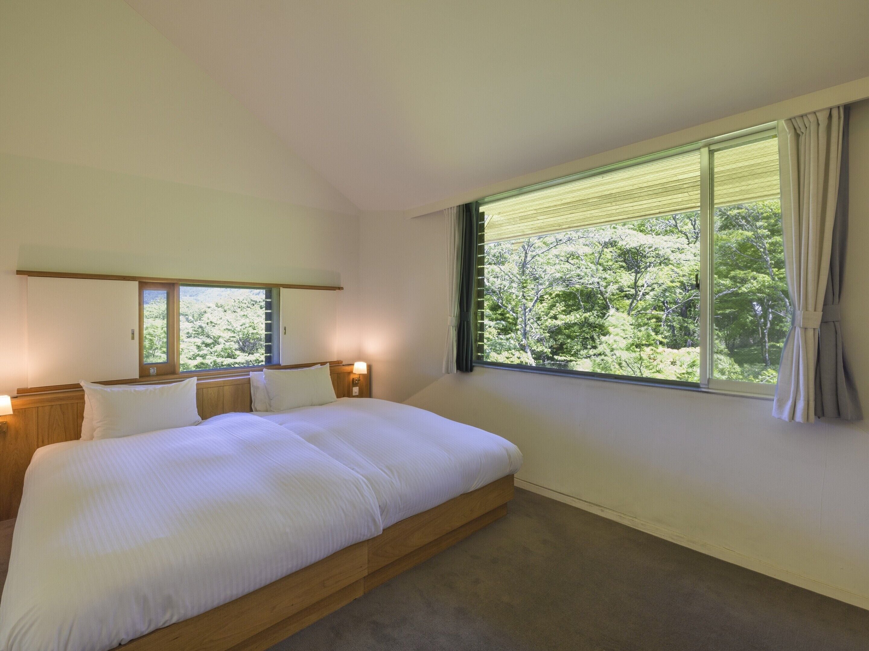 A bedroom with a large bed, two bedside tables, a window with curtains, and a view of trees.