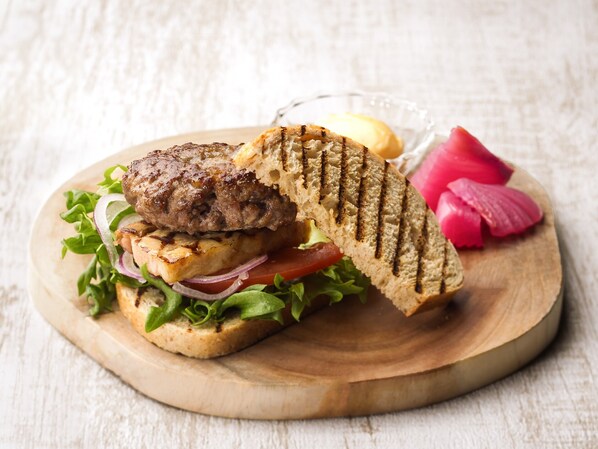 A grilled burger with lettuce, tomato, and onion on a wooden board. - Hakone Retreat Före (Hakone)