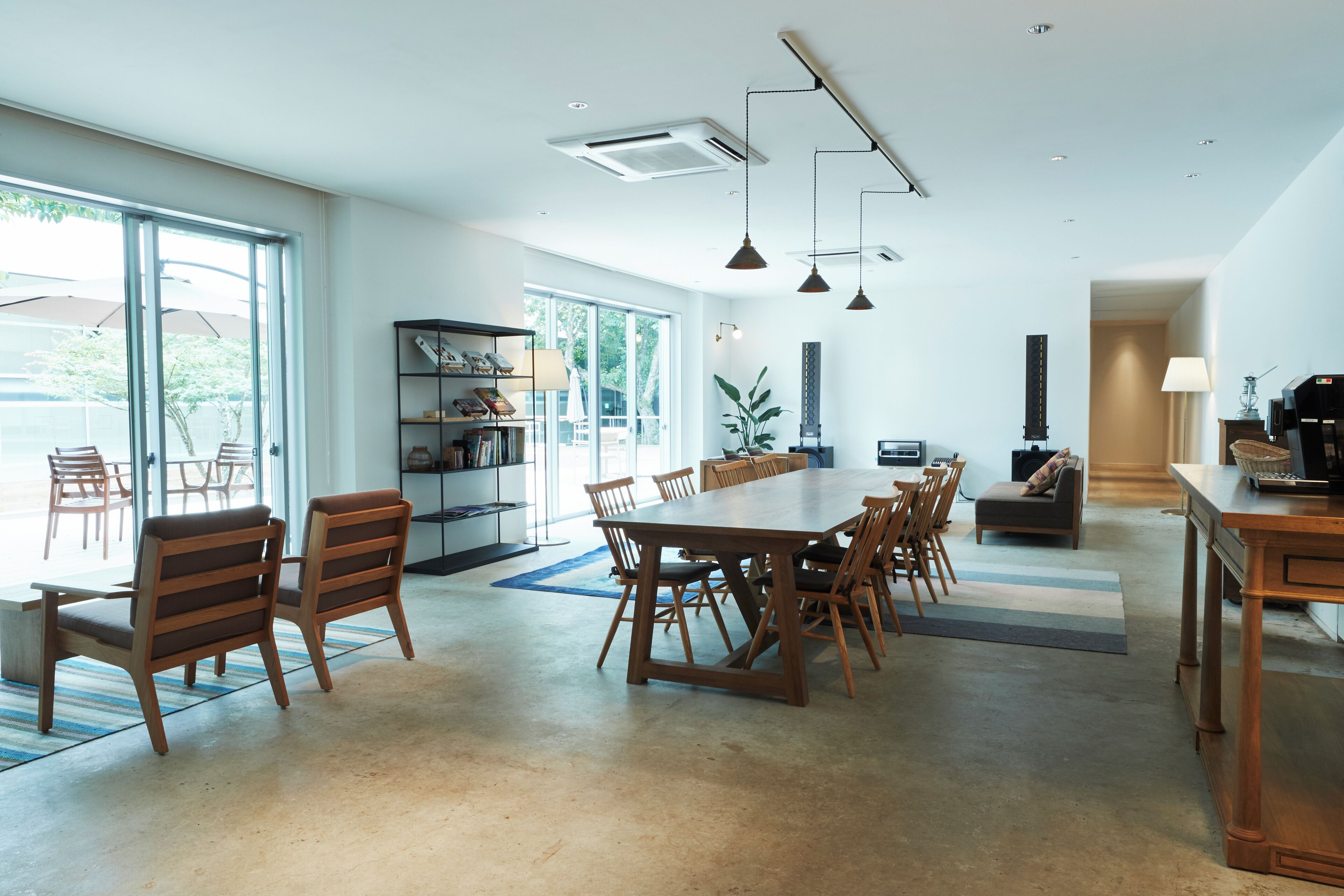 Un comedor amplio con una gran mesa y sillas de madera, una estantería y vistas a través de amplios ventanales.