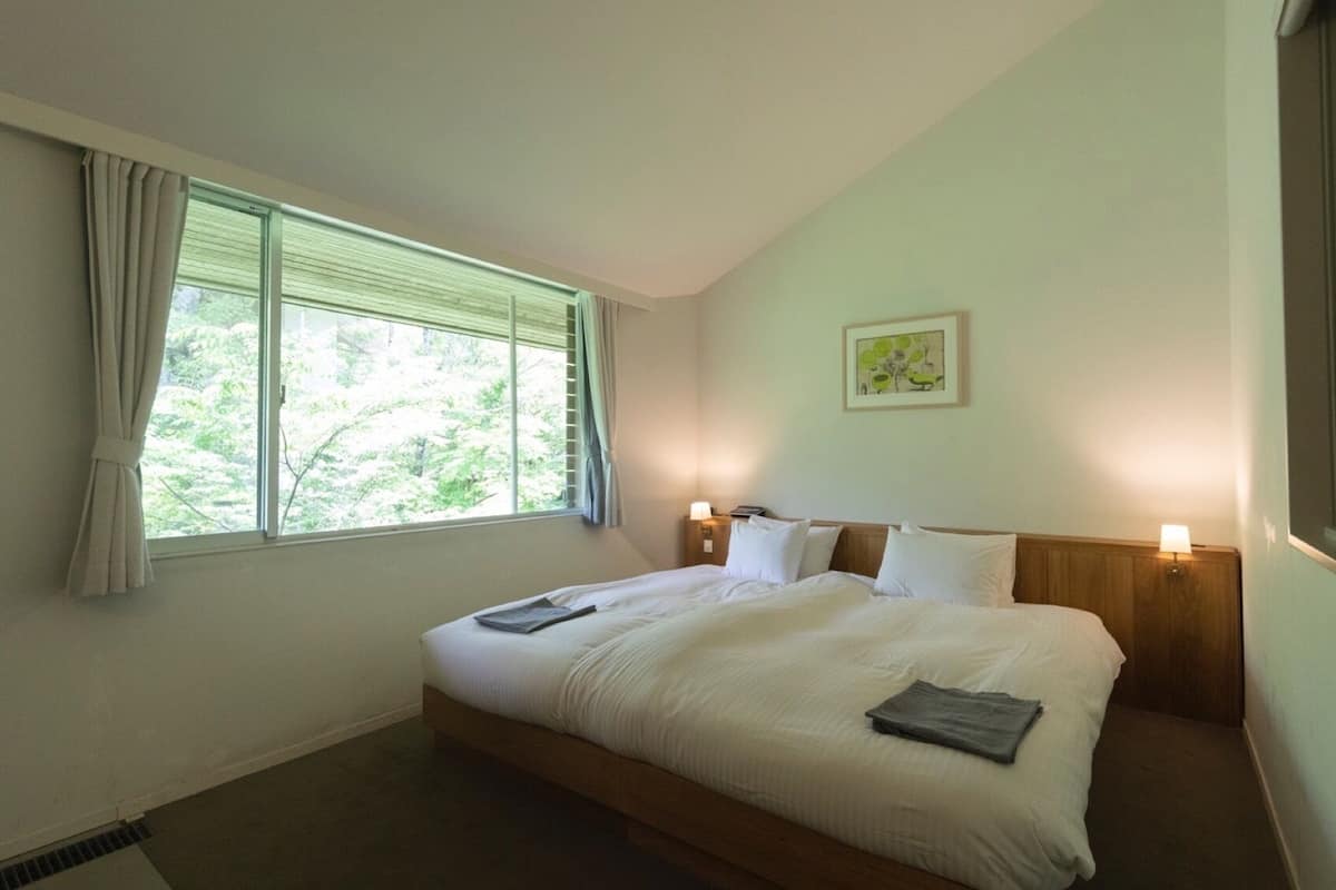 Habitación de hotel con una cama grande, una ventana con cortinas, una mesita de noche con una lámpara y un cuadro en la pared.