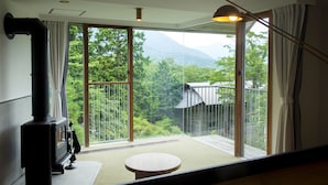 A modern room with a large sliding glass door leading to a balcony, a wood-burning stove, and a round wooden table. - Hakone Retreat Före (Hakone)