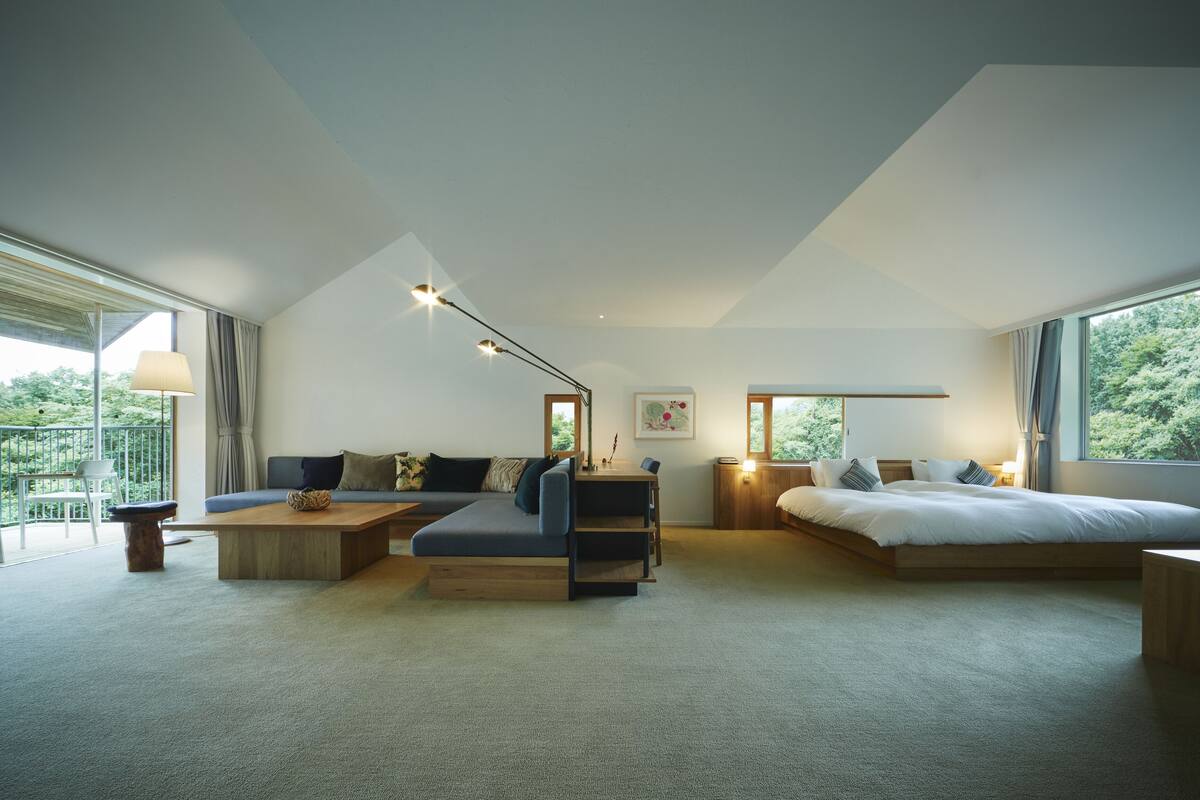 A modern bedroom with a sofa, a bed, a desk, and a large window.