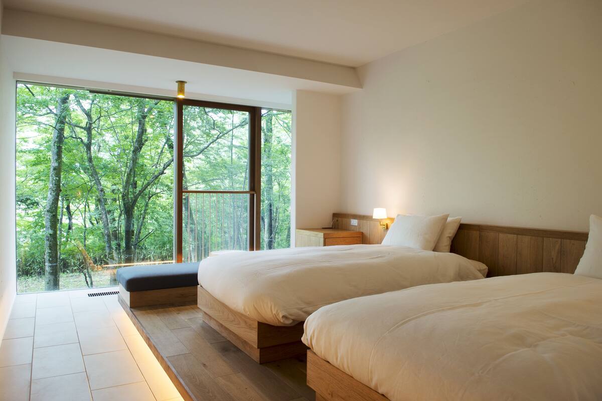 A bedroom with two beds, a large window, and a view of trees.