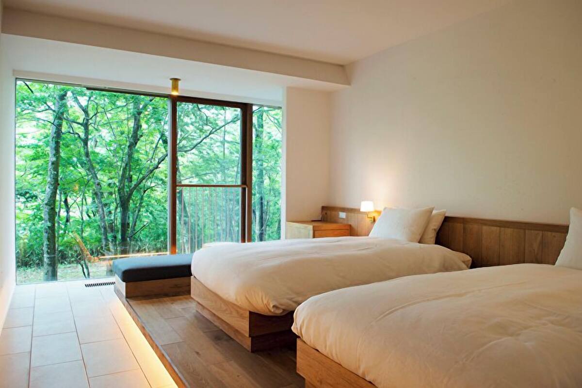 A bedroom with two beds, a large window, and a view of trees.