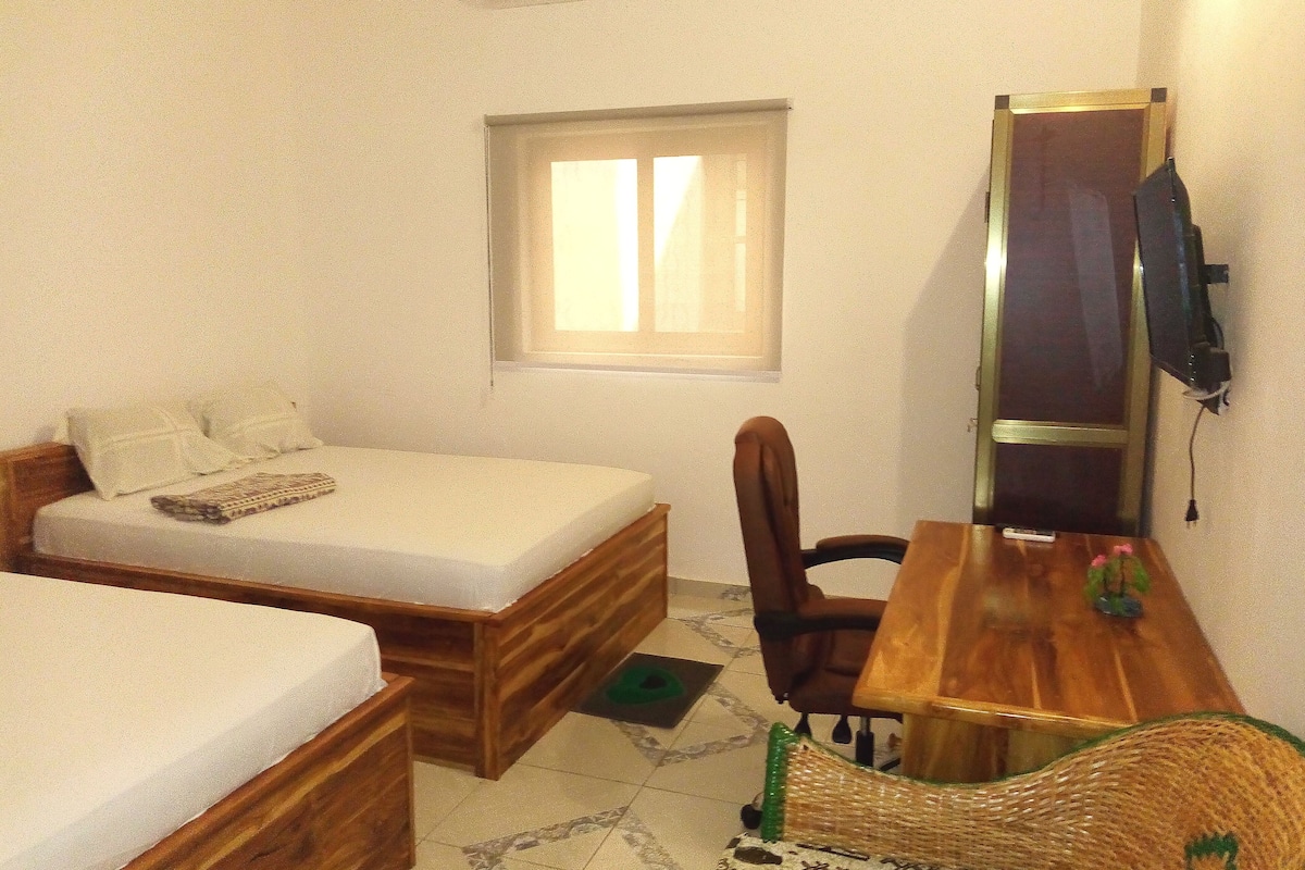A small room with a bed, a desk, a chair, a window, and a television.