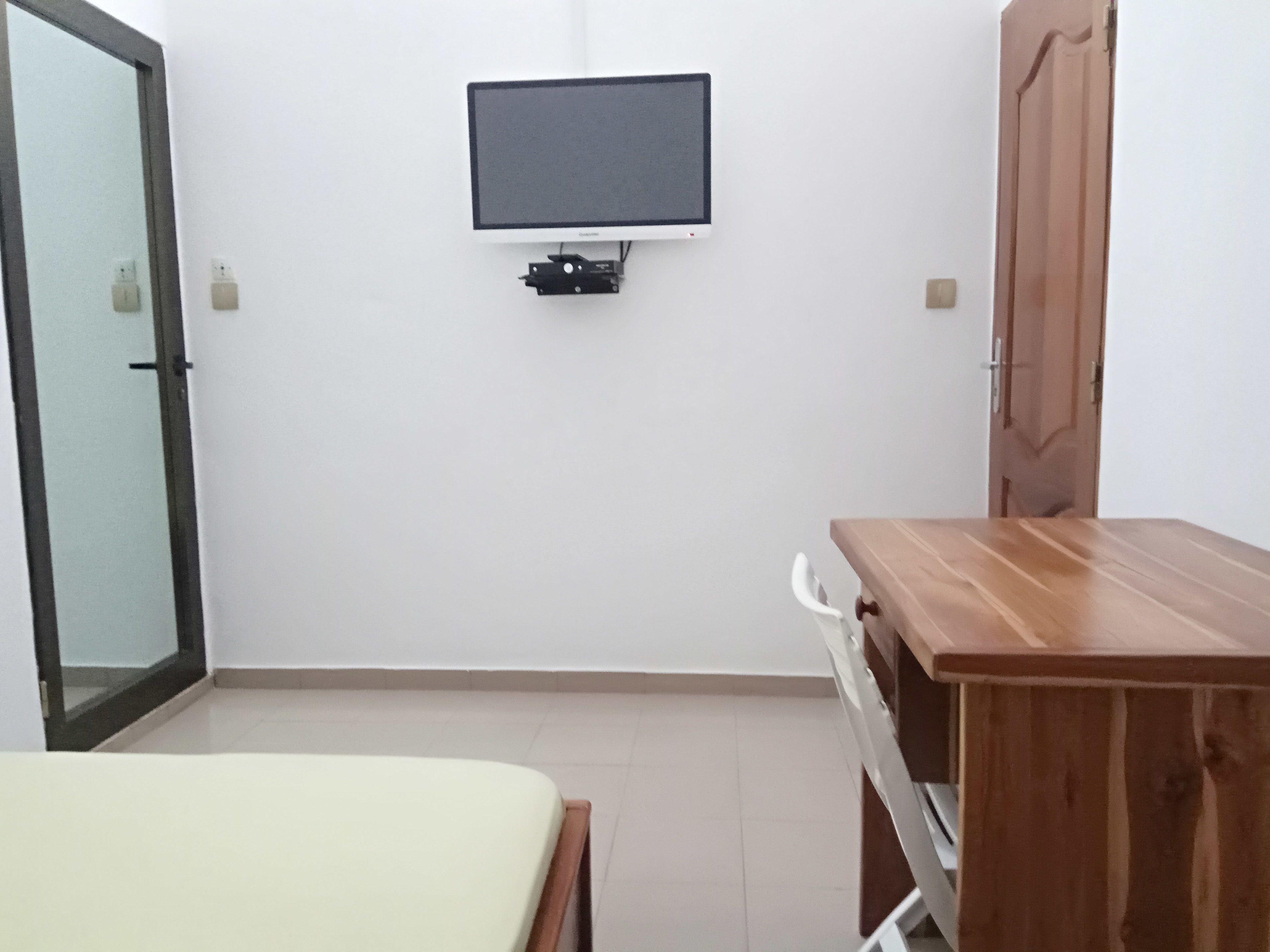 A room with a bed, a wooden desk, a television mounted on the wall, and a wardrobe.